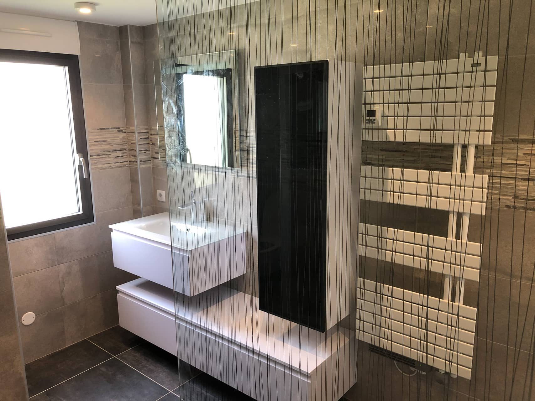 Salle de bains rénovée : meuble suspendu blanc, colonne noire, sèche-serviettes, paroi de douche sérigraphiée